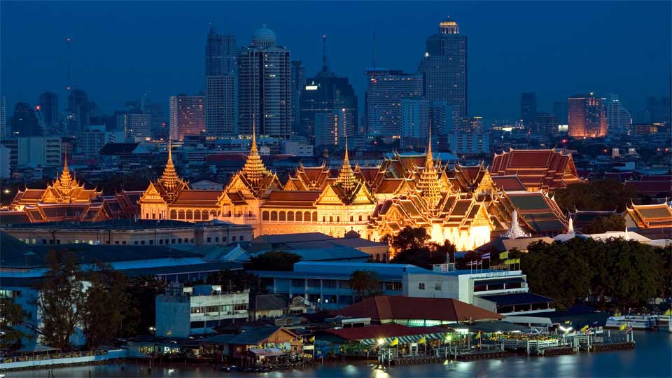 A wat lit up in gold light against the backdrop of Bangkok's skyline.