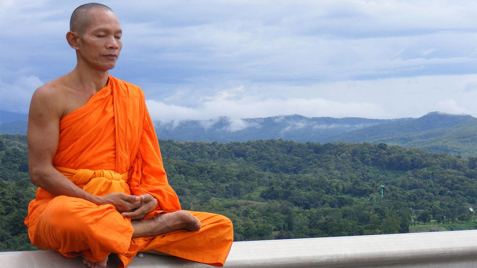 A Buddhist monk meditating on a railing overlooking misty mountains.