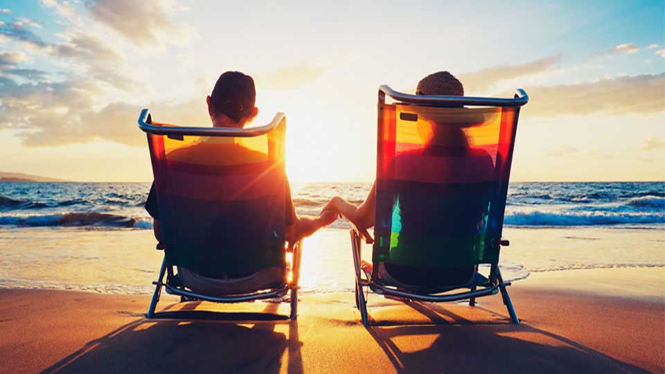 A couple holding hands, relaxing in lawn chairs on the beach at dawn or dusk.