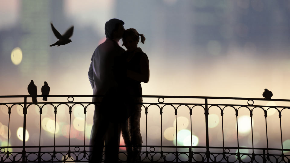 A romantic couple on a wrought iron bridge at night