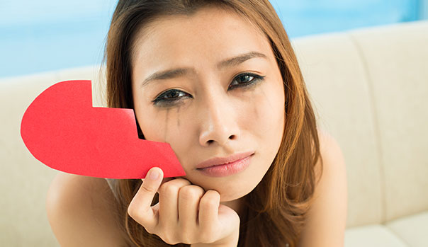 pretty girl crying holding a half of a paper heart