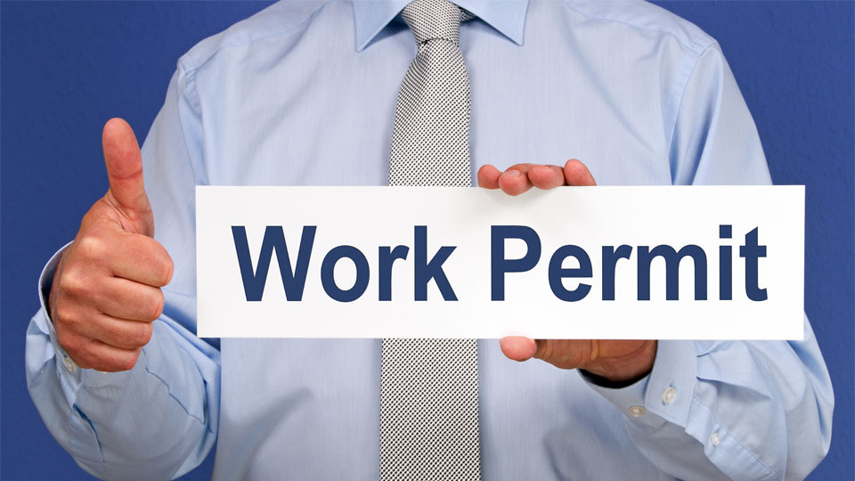 Man holding a sign reading "Work Permit" and giving a thumbs up